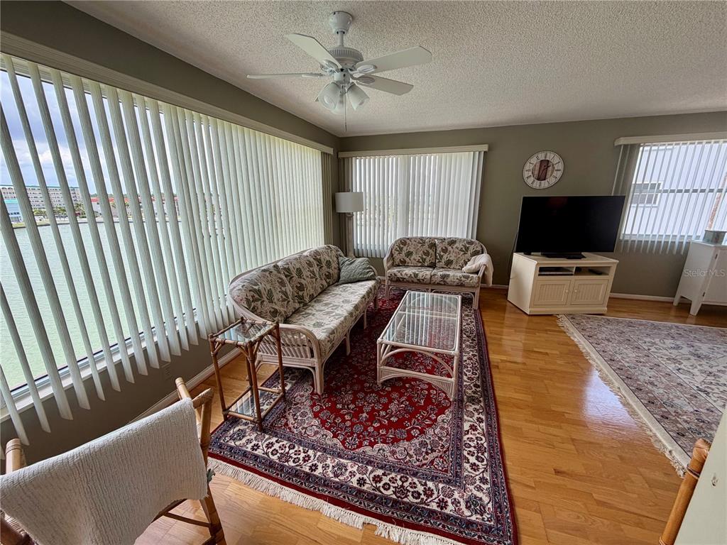 A living room features a red patterned rug, wicker furniture, and large windows with blinds — 6025 SHORE BOULEVARD S UNIT 415, GULFPORT, FL