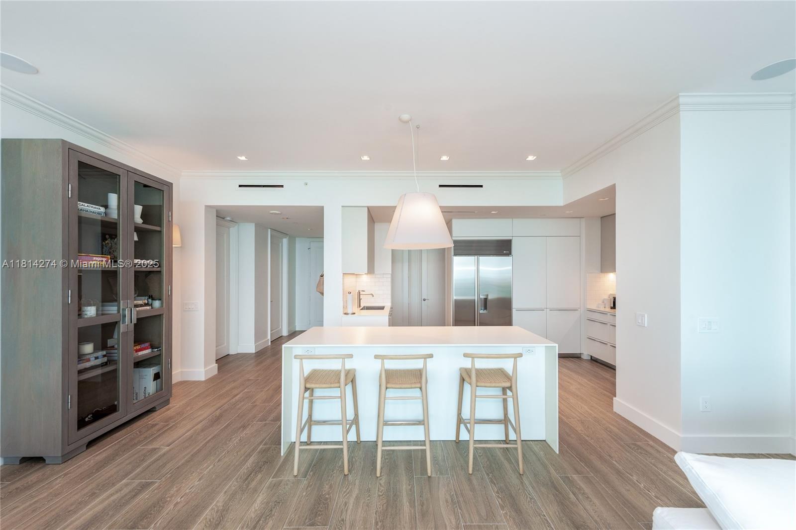 A modern kitchen features a white island with three wooden stools and light wood flooring — 10295 Collins Ave # 2506, Bal Harbour FL 33154, BAL HARBOUR, FL