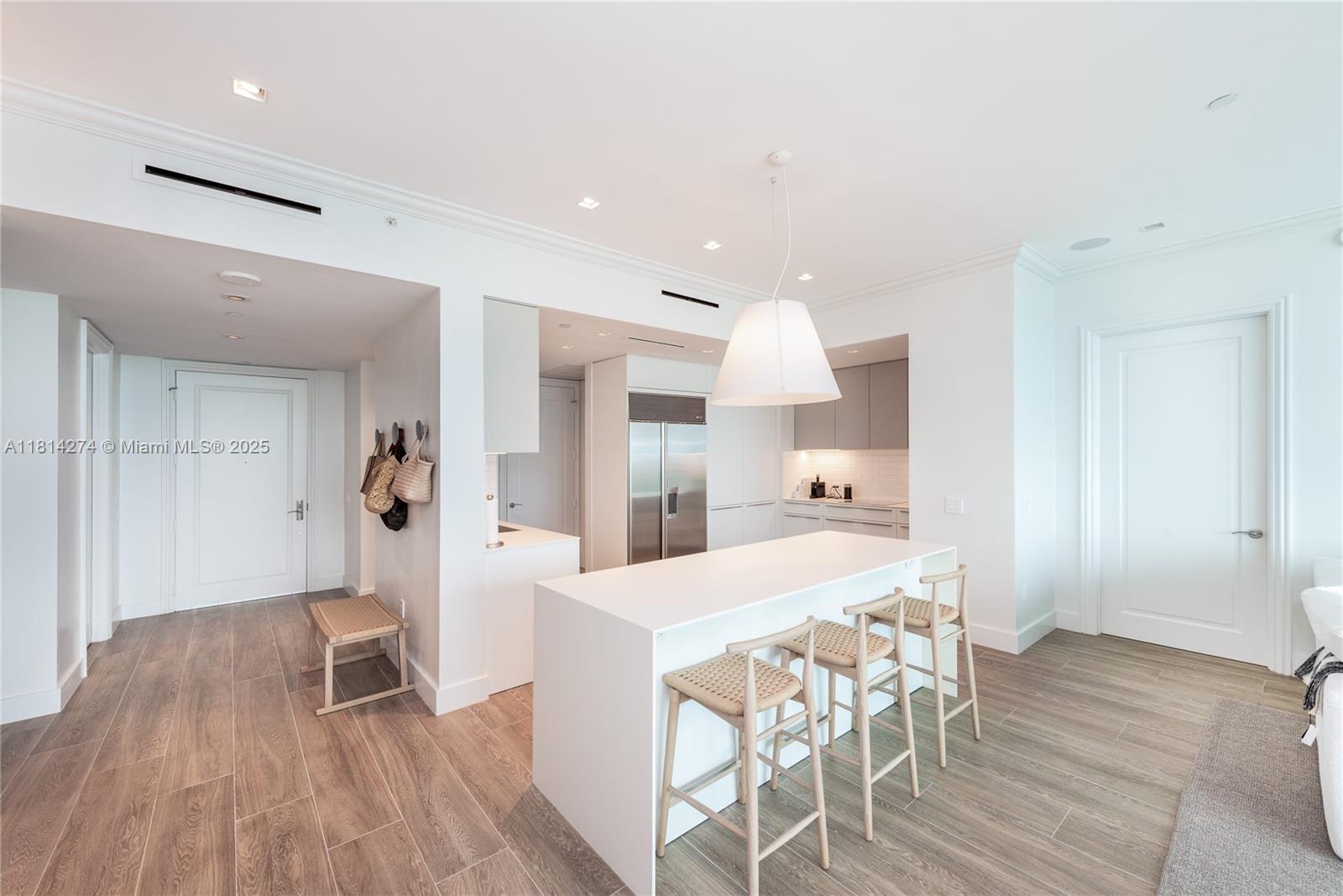 A modern kitchen features a white island with three stools and light wood flooring — 10295 Collins Ave # 2506, Bal Harbour FL 33154, BAL HARBOUR, FL