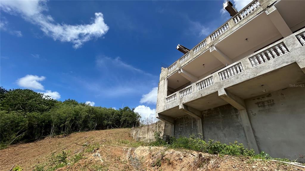 A multi-story concrete building stands on a sloped, partially cleared hillside under a blue sky — 557 VILLA BORINQUEN, VIEQUES, PR