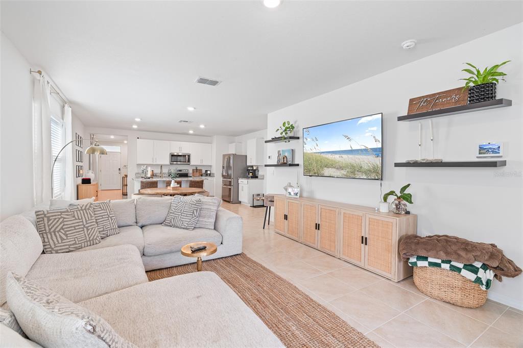 A living room with a sectional sofa, television, and open kitchen in the background — 365 CARYOTA COURT, NEW SMYRNA BEACH, FL