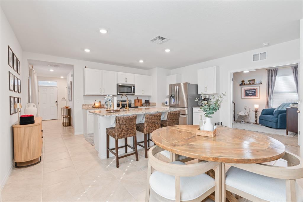 A kitchen with white cabinets, granite countertops, and an island with three woven bar stools — 365 CARYOTA COURT, NEW SMYRNA BEACH, FL