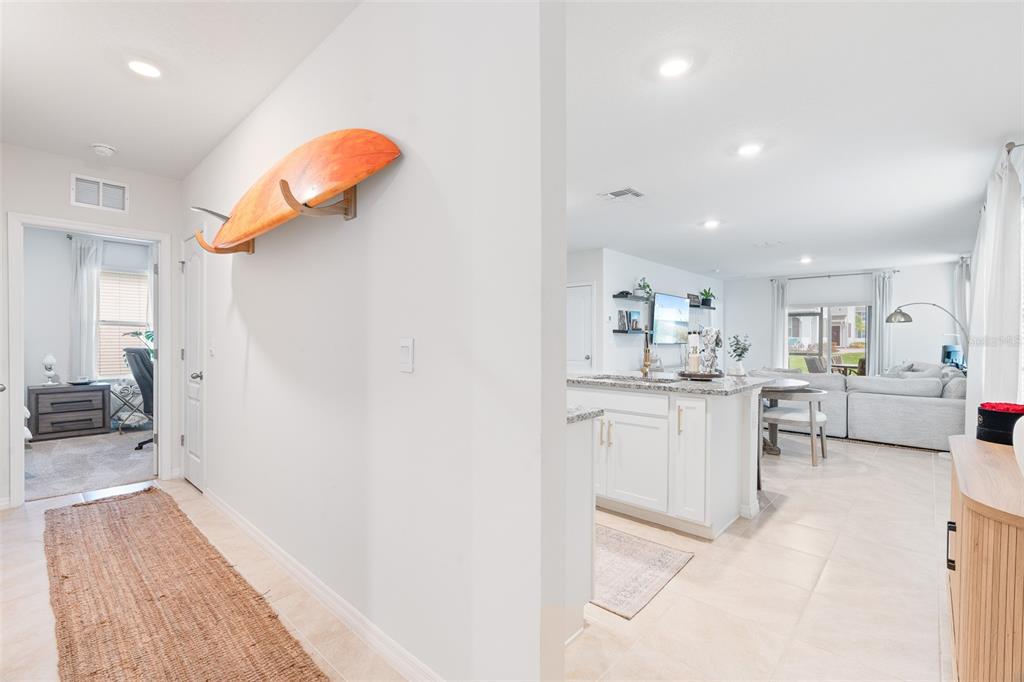 A hallway with a surfboard wall mount leads into an open-concept kitchen and living area — 365 CARYOTA COURT, NEW SMYRNA BEACH, FL