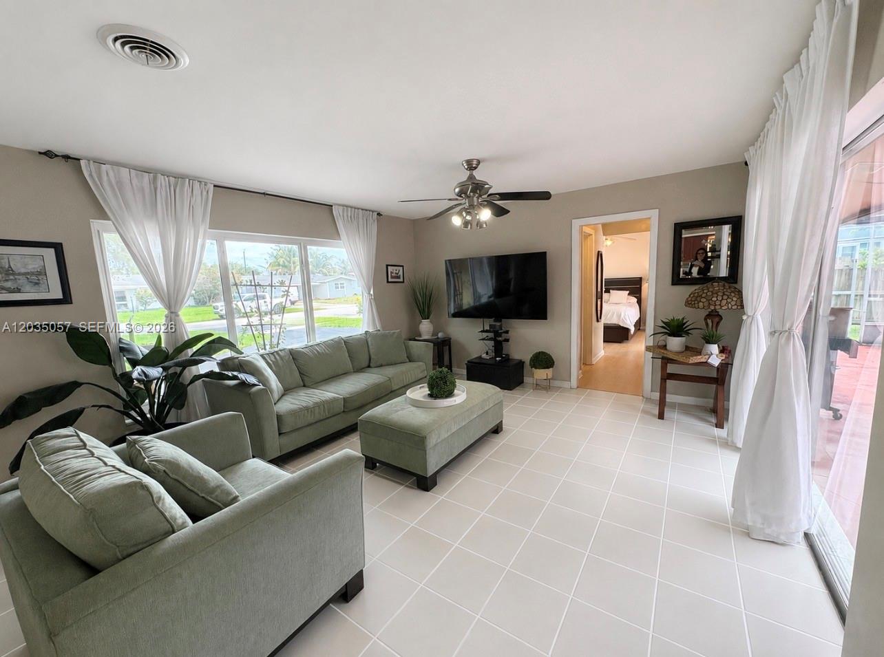 A living room features light green furniture, tile flooring, and large windows with white curtains — 1812 N 45th Ave, Hollywood FL 33021, HOLLYWOOD, FL