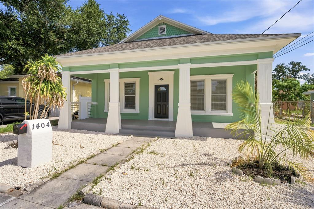 A green single-story house features a covered front porch with white columns and gravel landscaping — 1404 E 26TH AVENUE, TAMPA, FL