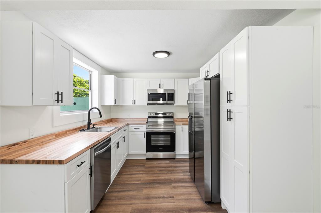 A kitchen features white cabinets, butcher block countertops, stainless steel appliances, and wood-look flooring — 1404 E 26TH AVENUE, TAMPA, FL