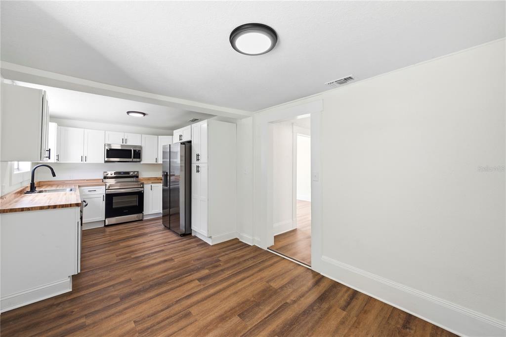A kitchen with white cabinets, stainless steel appliances, and wood-look flooring opens to a hallway — 1404 E 26TH AVENUE, TAMPA, FL