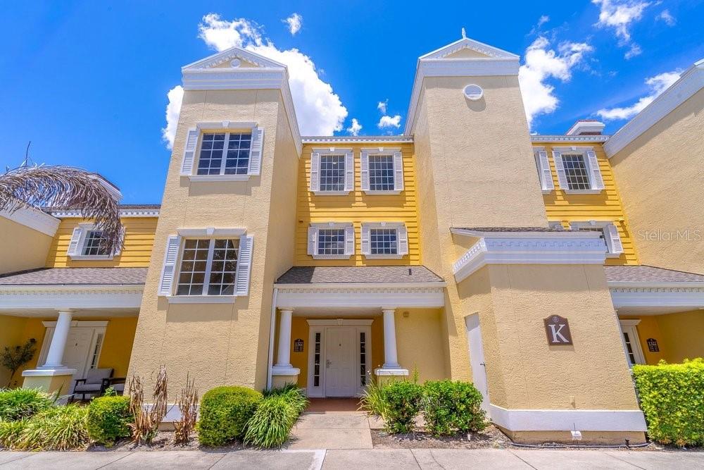 A yellow multi-story residential building features white trim, multiple windows, and a covered entryway — 1322 SEVEN EAGLES COURT UNIT 302, REUNION, FL