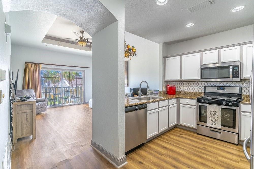 A kitchen with white cabinets and granite countertops opens into a living area with balcony access — 1322 SEVEN EAGLES COURT UNIT 302, REUNION, FL