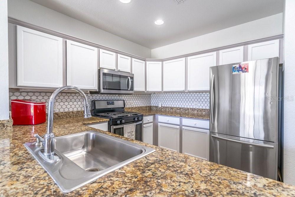 A kitchen features white cabinets, granite countertops, stainless steel appliances, and a tiled backsplash — 1322 SEVEN EAGLES COURT UNIT 302, REUNION, FL