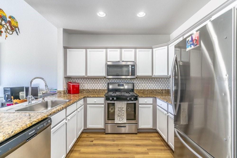 A kitchen with white cabinets, stainless steel appliances, granite countertops, and a patterned tile backsplash — 1322 SEVEN EAGLES COURT UNIT 302, REUNION, FL