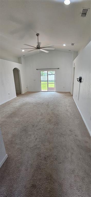 A spacious living room features beige carpeting, a vaulted ceiling with a fan, and sliding doors — 240 SOLIS DRIVE, WINTER HAVEN, FL