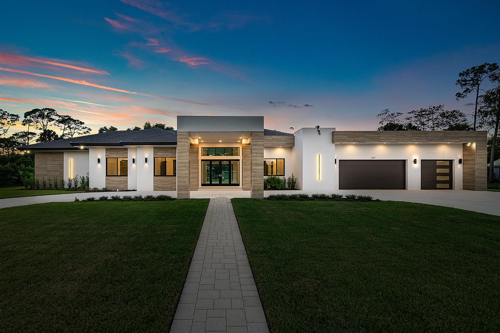 A modern single-story house with a stone-accented entryway, dark garage doors, and a paved walkway — 14817 Paddock Drive, Wellington FL 33414, WELLINGTON, FL