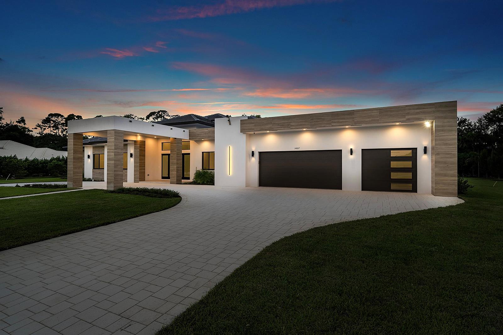 A modern single-story house with a paved driveway, wood-look accents, and a three-car garage — 14817 Paddock Drive, Wellington FL 33414, WELLINGTON, FL