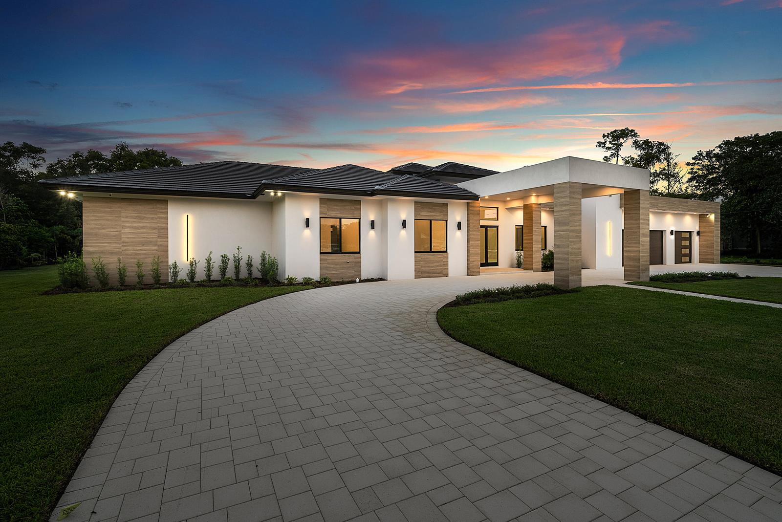 A modern single-story house with a paved driveway, wood-look accents, and a covered entryway at dusk — 14817 Paddock Drive, Wellington FL 33414, WELLINGTON, FL