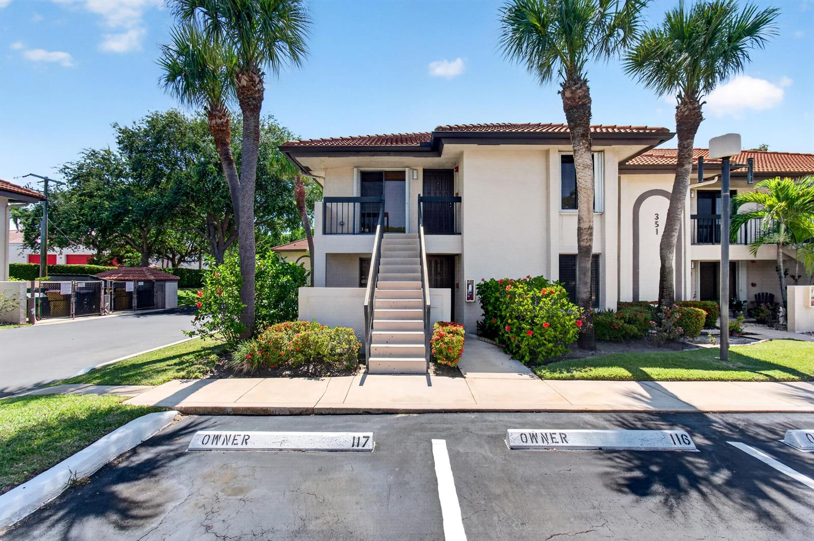 A two-story apartment building exterior features a central staircase, palm trees, and assigned parking spaces — 351 Club Circle # 101, Boca Raton FL 33487, BOCA RATON, FL