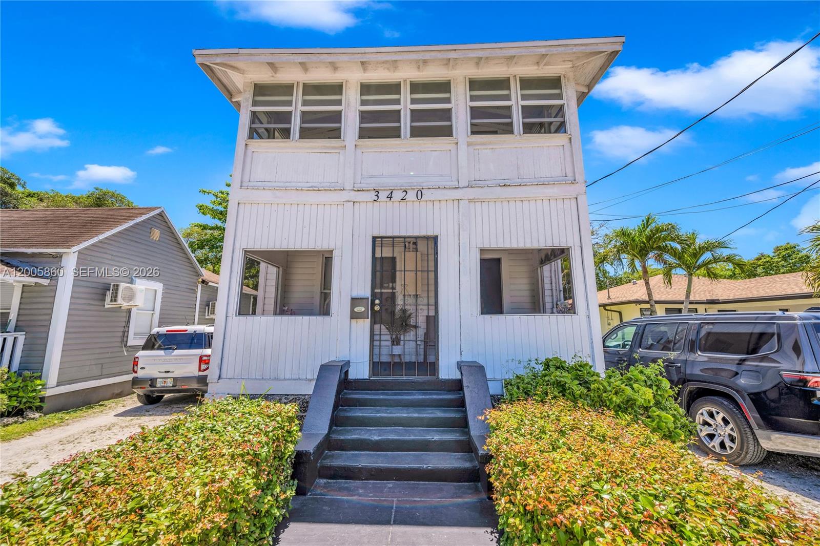 A two-story white house with vertical siding features a central staircase and screened-in porches — 3420 Charles Ave, Miami FL 33133, MIAMI, FL