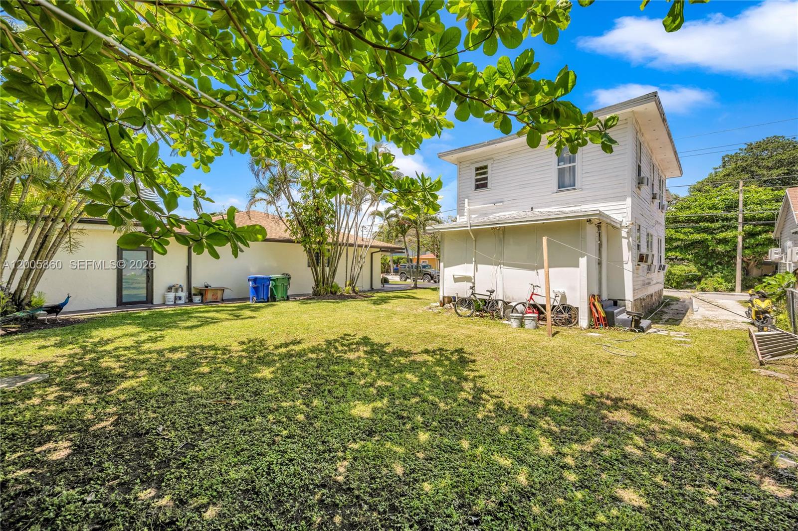 A grassy backyard features a two-story white house, a single-story building, and several bicycles — 3420 Charles Ave, Miami FL 33133, MIAMI, FL