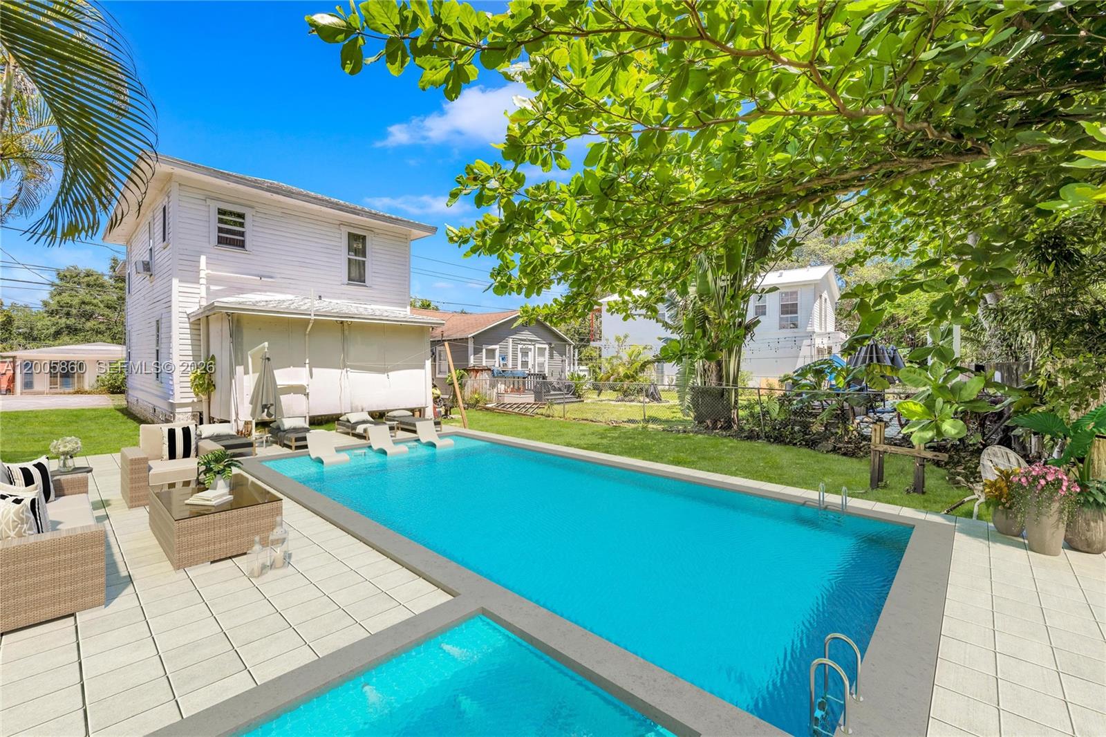 A backyard features a rectangular swimming pool with a spa, patio furniture, and white house — 3420 Charles Ave, Miami FL 33133, MIAMI, FL