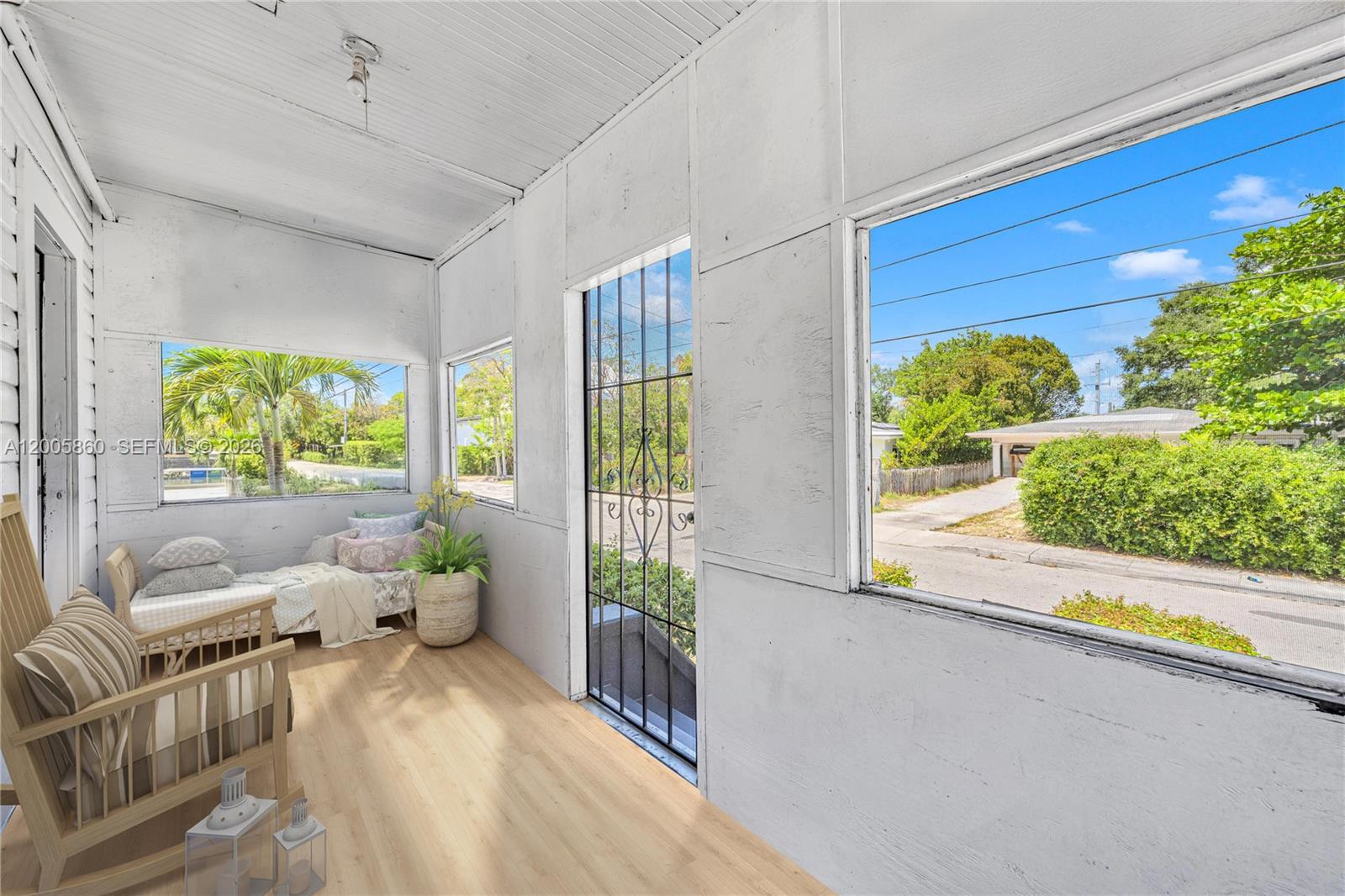 A sunroom features light wood flooring, white paneled walls, and large windows overlooking a street — 3420 Charles Ave, Miami FL 33133, MIAMI, FL