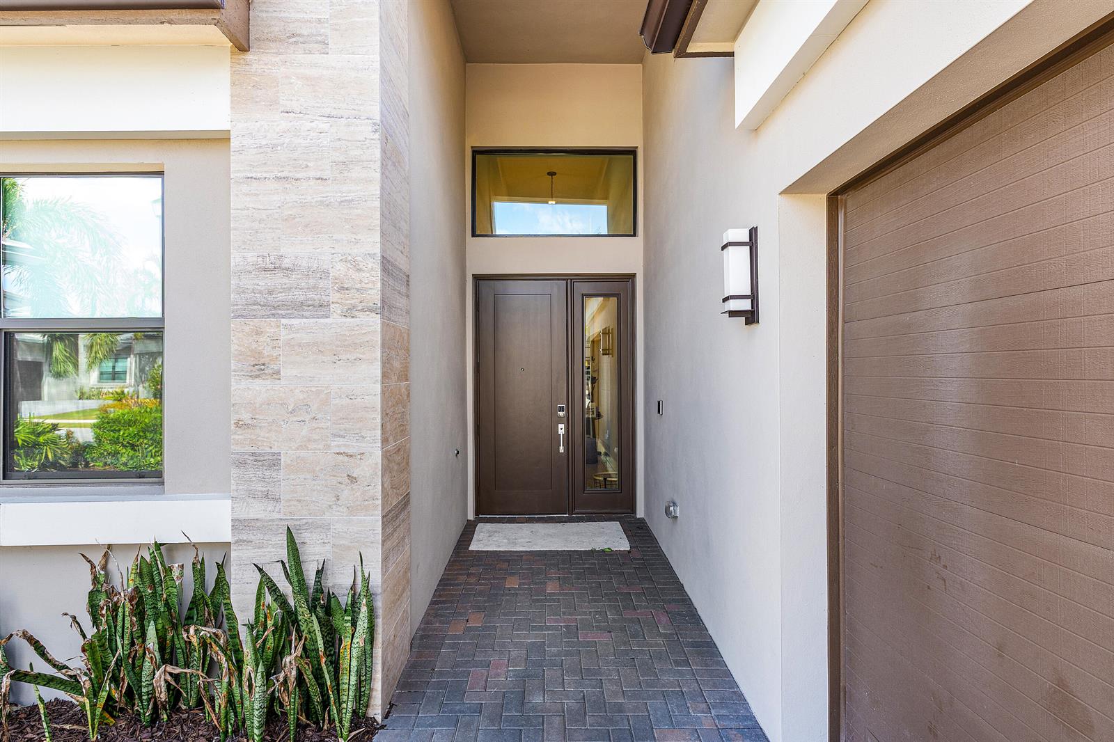 A modern home entryway features a dark wood front door, stone siding, and brick pavers — 9212 Silver Marsh Lane, Boca Raton FL 33434, BOCA RATON, FL