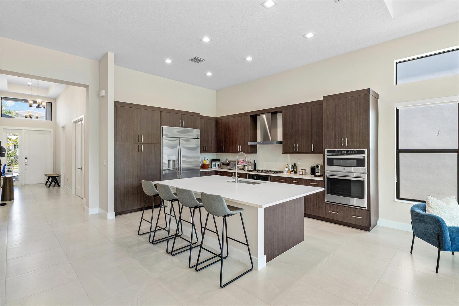 A modern kitchen features dark wood cabinetry, a large white island, and stainless steel appliances — 9212 Silver Marsh Lane, Boca Raton FL 33434, BOCA RATON, FL