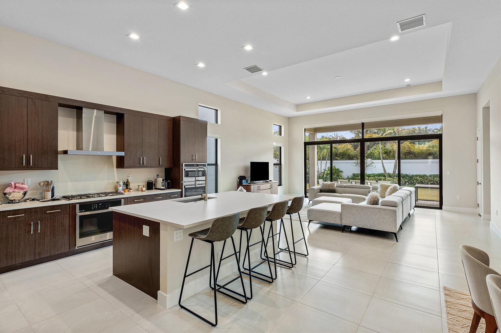 A modern open-concept kitchen and living area features dark wood cabinetry, a large island, and floor-to-ceiling windows — 9212 Silver Marsh Lane, Boca Raton FL 33434, BOCA RATON, FL