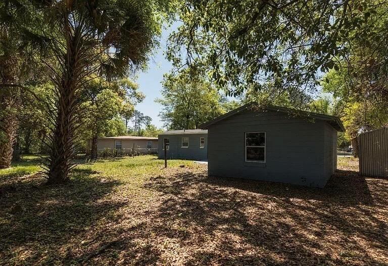 A grassy backyard features two small, grey-painted buildings shaded by large trees — 2513 Spirea Street, Jacksonville FL 32209, JACKSONVILLE, FL