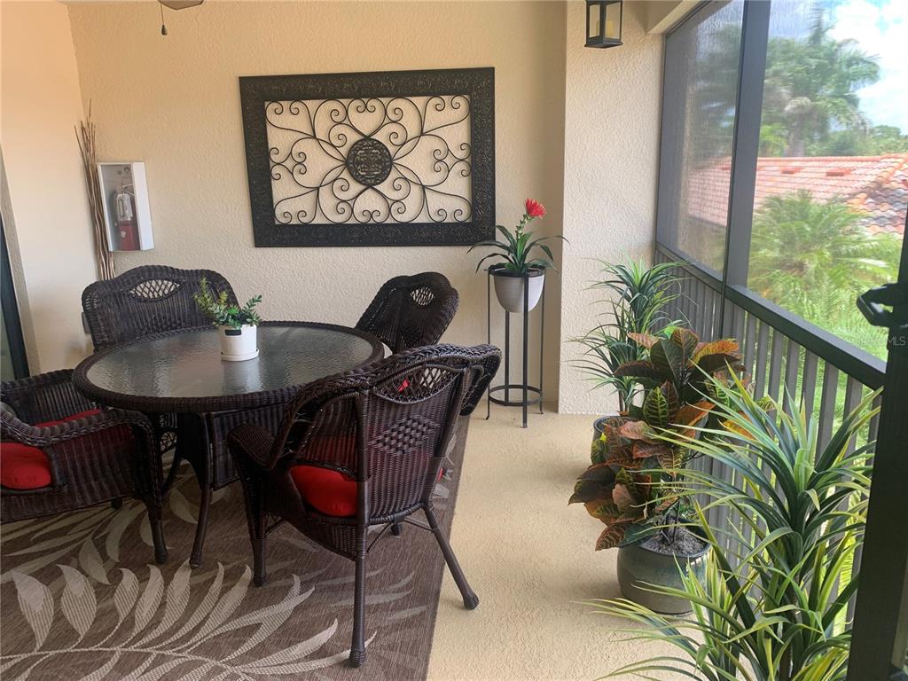 A screened-in balcony features a round wicker dining set, potted plants, and wall decor — 7225 RIVER HAMMOCK DRIVE UNIT 202, BRADENTON, FL