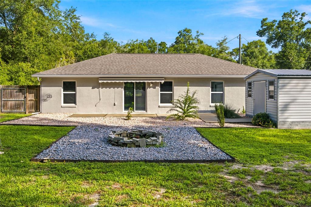 The backyard of a single-story house features a gravel patio, fire pit, and storage shed — 19056 SAINT BENEDICT DRIVE, DUNNELLON, FL