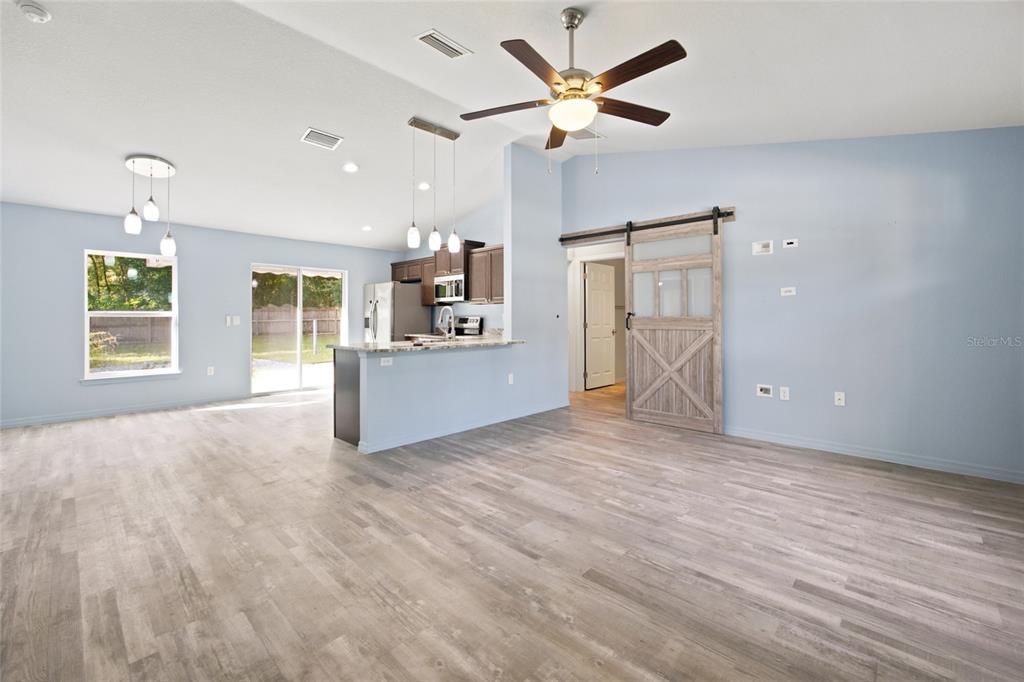 An open-concept living area features light blue walls, wood-look flooring, a kitchen island, and a barn door — 19056 SAINT BENEDICT DRIVE, DUNNELLON, FL