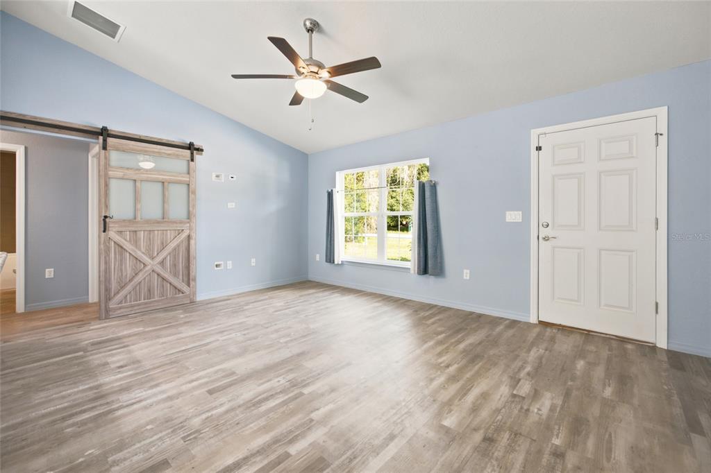 A room with light blue walls, wood-look flooring, a ceiling fan, and a sliding barn door — 19056 SAINT BENEDICT DRIVE, DUNNELLON, FL