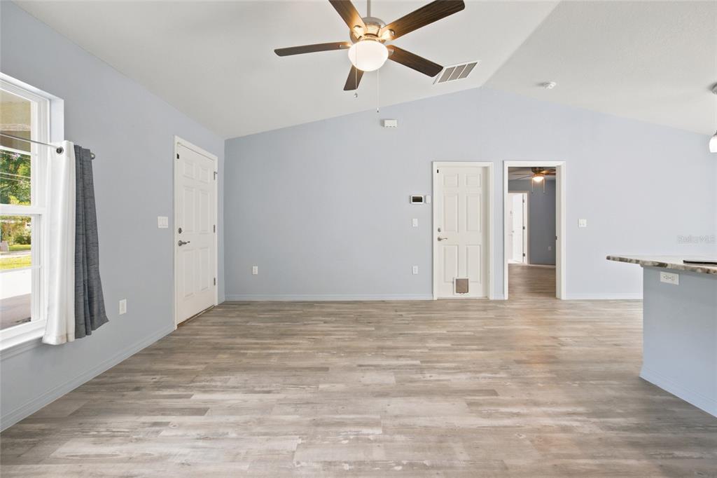 A living room with light blue walls, wood-look flooring, a ceiling fan, and two doors — 19056 SAINT BENEDICT DRIVE, DUNNELLON, FL
