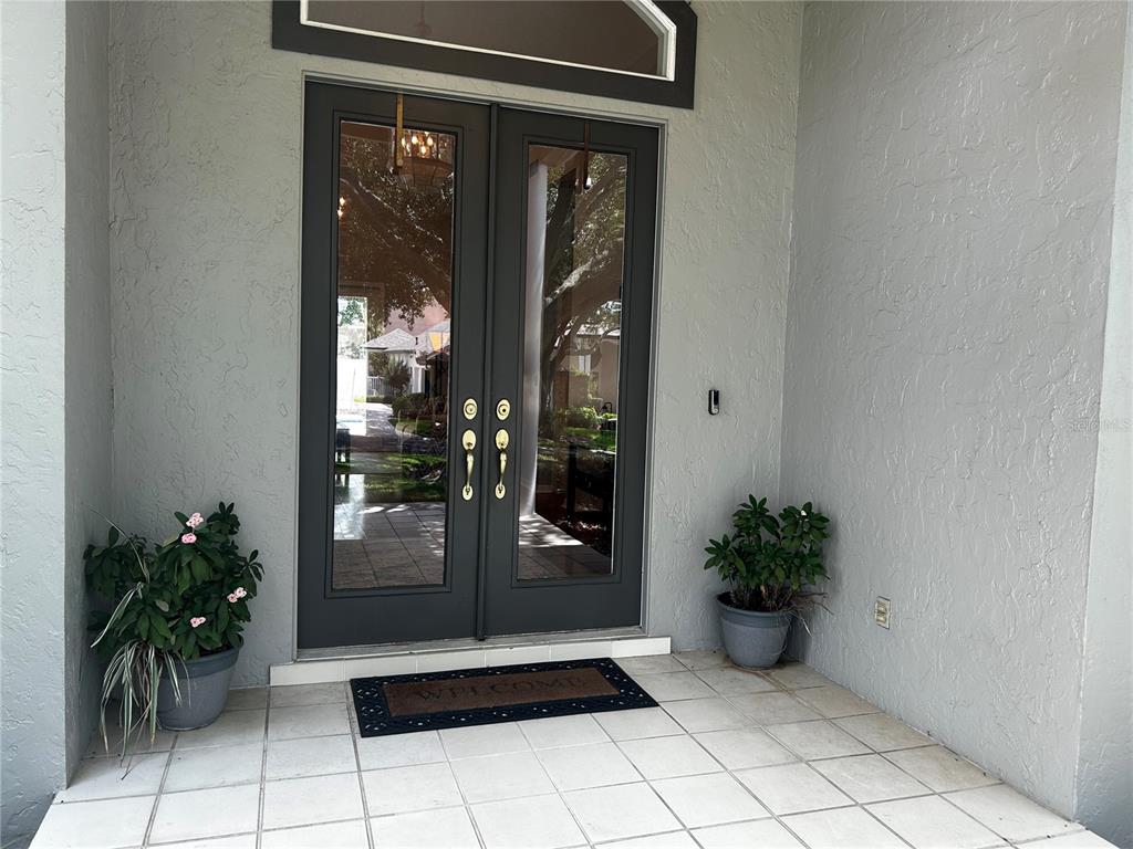 A gray double front door with glass panels sits on a tiled porch with potted plants — 936 HAMILTON PLACE DRIVE, LAKELAND, FL