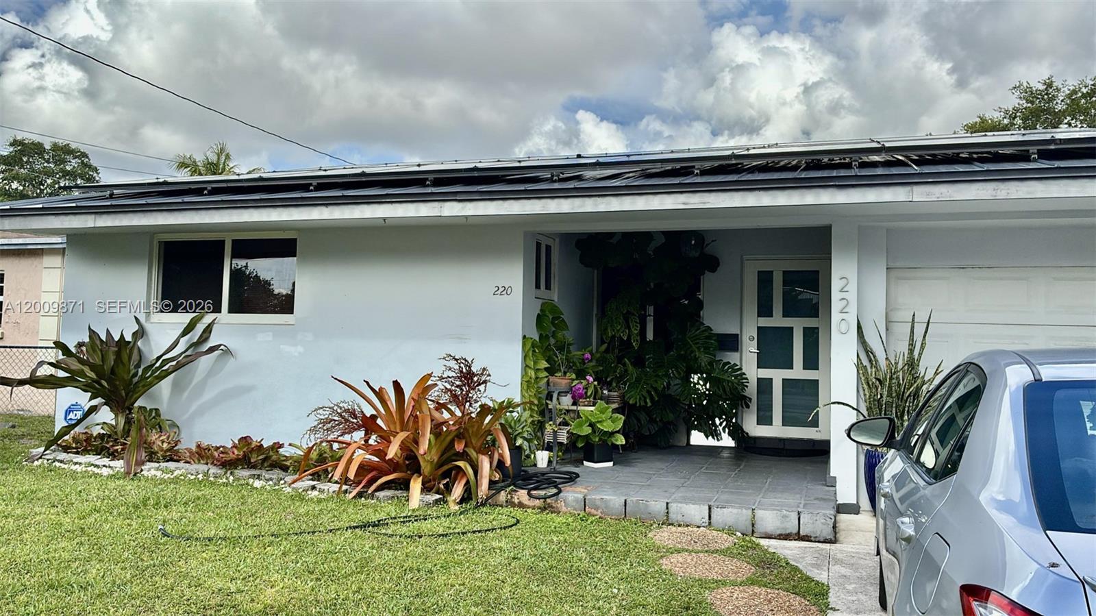 The exterior of a single-story house features a light blue facade, solar panels, and landscaping — 220 SW 3rd Ave # 0, Hallandale Beach FL 33009, HALLANDALE BEACH, FL