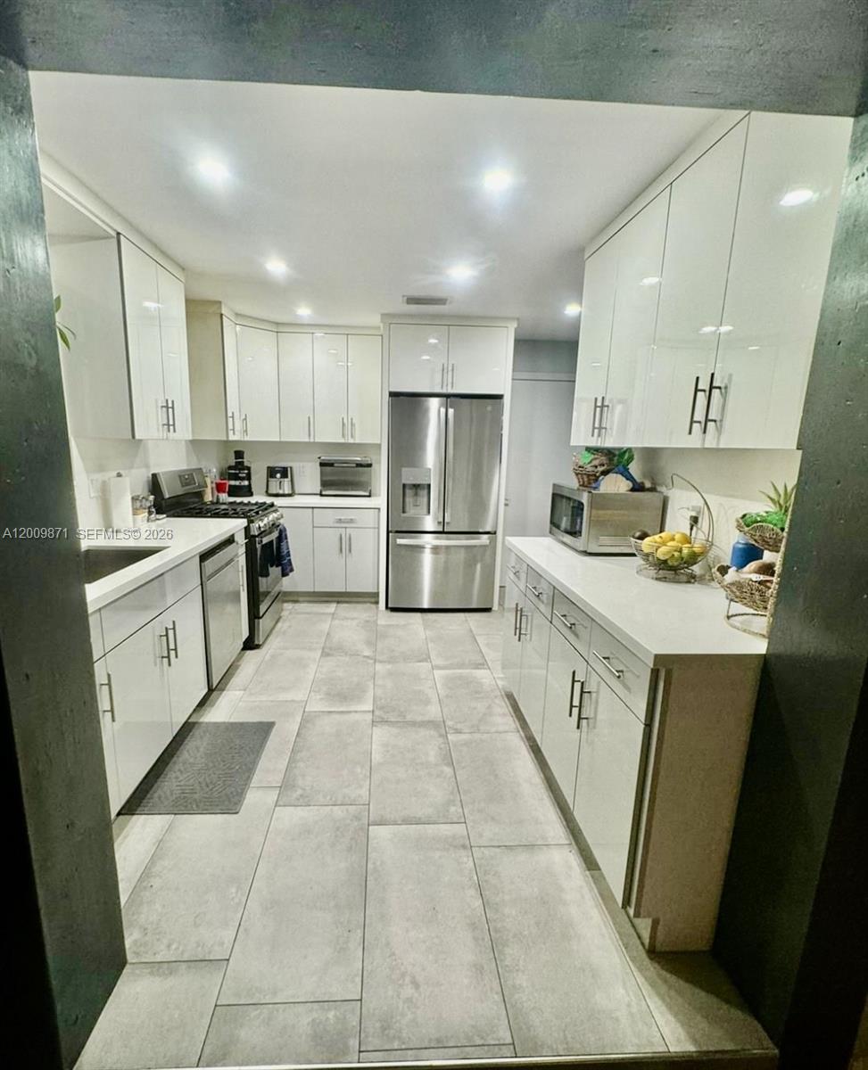 A galley kitchen features white cabinets, stainless steel appliances, and light gray tile flooring — 220 SW 3rd Ave # 0, Hallandale Beach FL 33009, HALLANDALE BEACH, FL