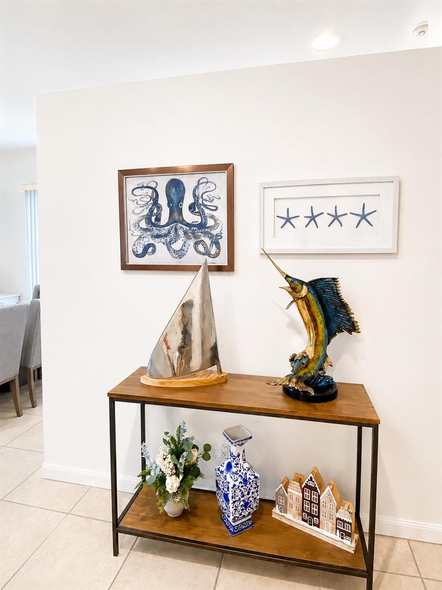 A console table displays nautical decor beneath framed artwork on a white wall — 7529 SE Bay Cedar Circle, Hobe Sound FL 33455, HOBE SOUND, FL