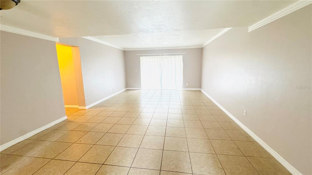 An empty living room features light-colored walls, crown molding, and beige tile flooring — 5508 POKEWEED COURT UNIT 146, TAMPA, FL