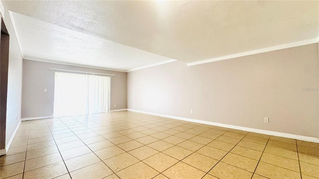 An empty living room features beige tile flooring, light-colored walls, and sliding glass patio doors — 5508 POKEWEED COURT UNIT 146, TAMPA, FL