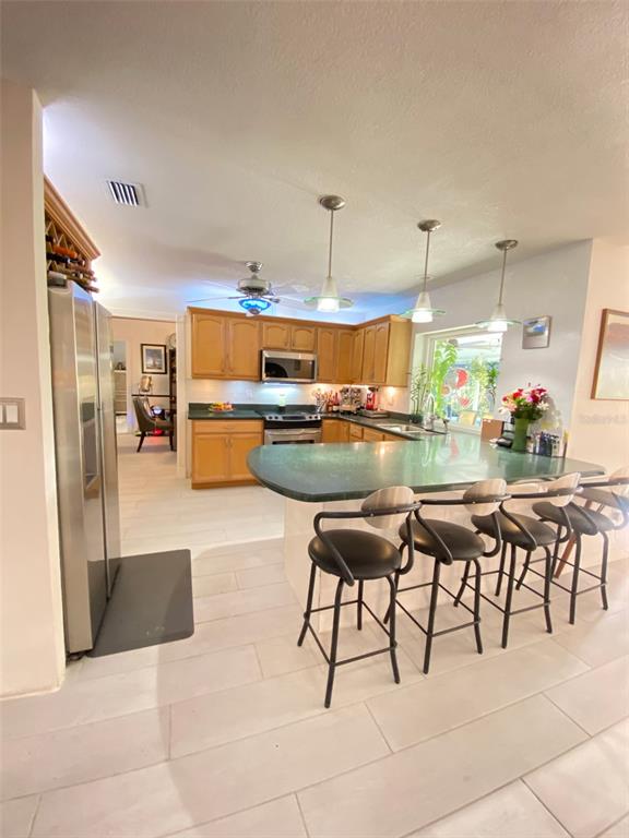 A kitchen features wood cabinets, a green countertop island, and three black bar stools — 4076 SOUTHWELL WAY, SARASOTA, FL