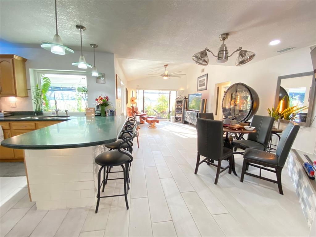 An open-concept kitchen and dining area features a breakfast bar, tile flooring, and large windows — 4076 SOUTHWELL WAY, SARASOTA, FL