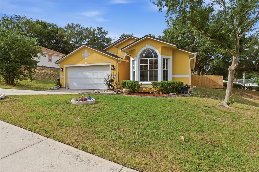 A yellow single-story house features a two-car garage, an arched window, and a front lawn — 1514 MUIR CIRCLE, CLERMONT, FL