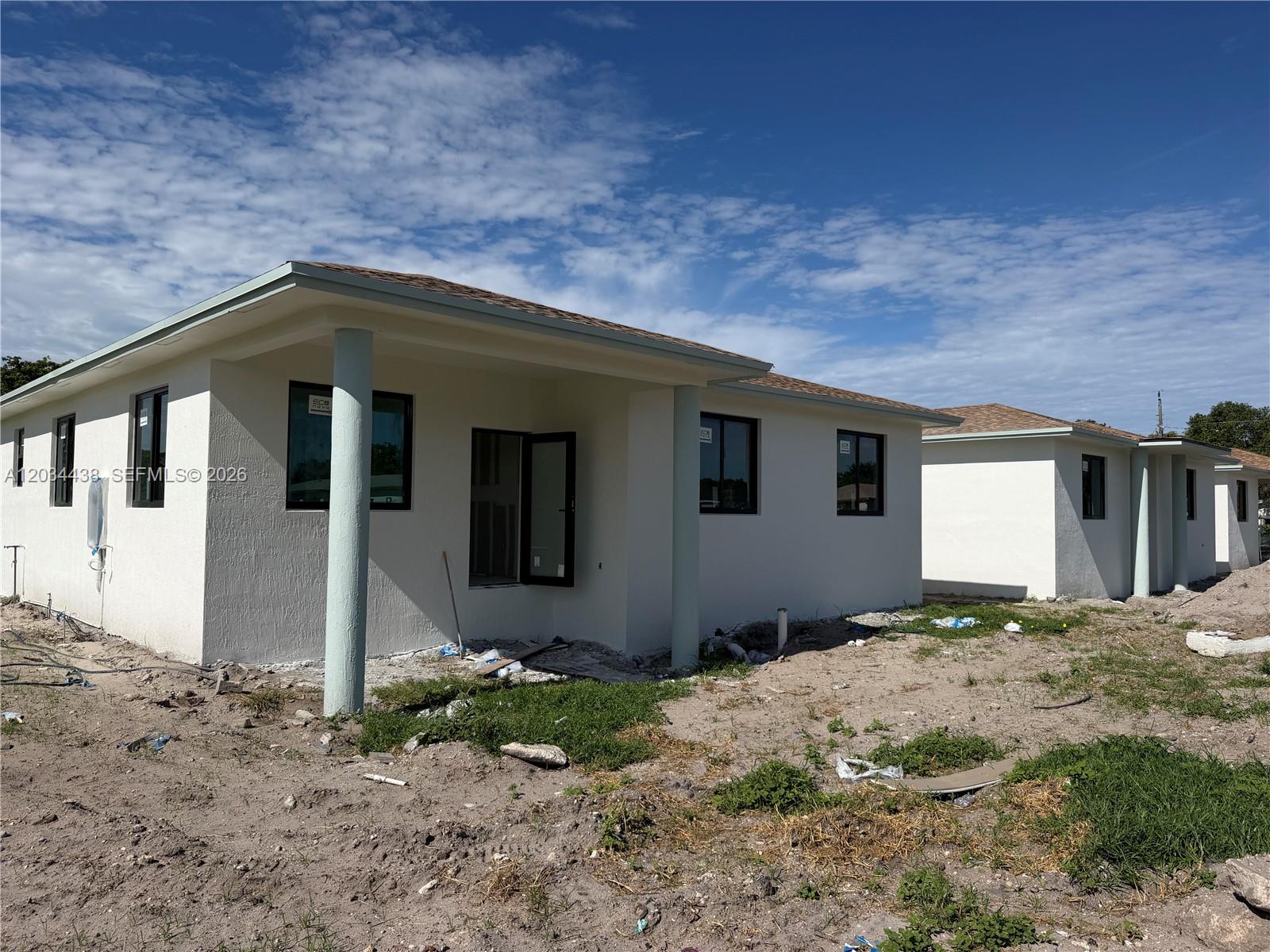 Two newly constructed, white stucco houses stand on a dirt lot under a blue sky — 336 NW 11th St, Pompano Beach FL 33060, POMPANO BEACH, FL