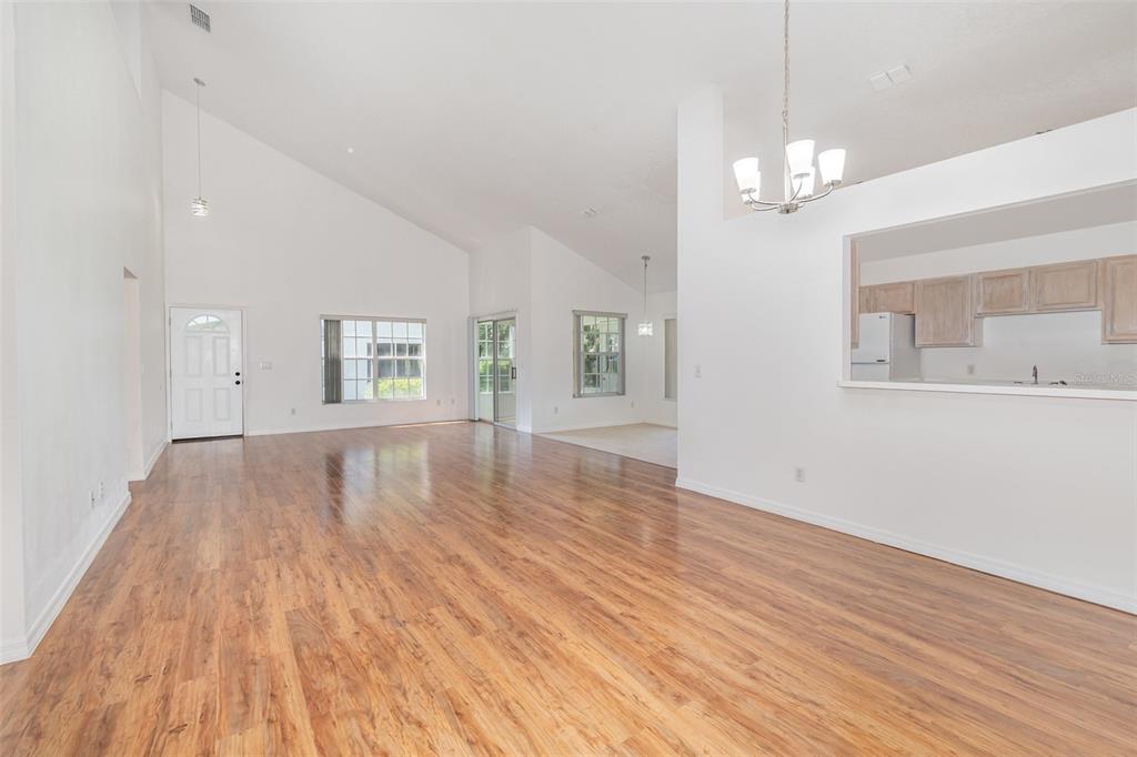 A spacious living area with vaulted ceilings, wood-look flooring, and an open kitchen pass-through window — 2548 ALBION AVENUE, ORLANDO, FL