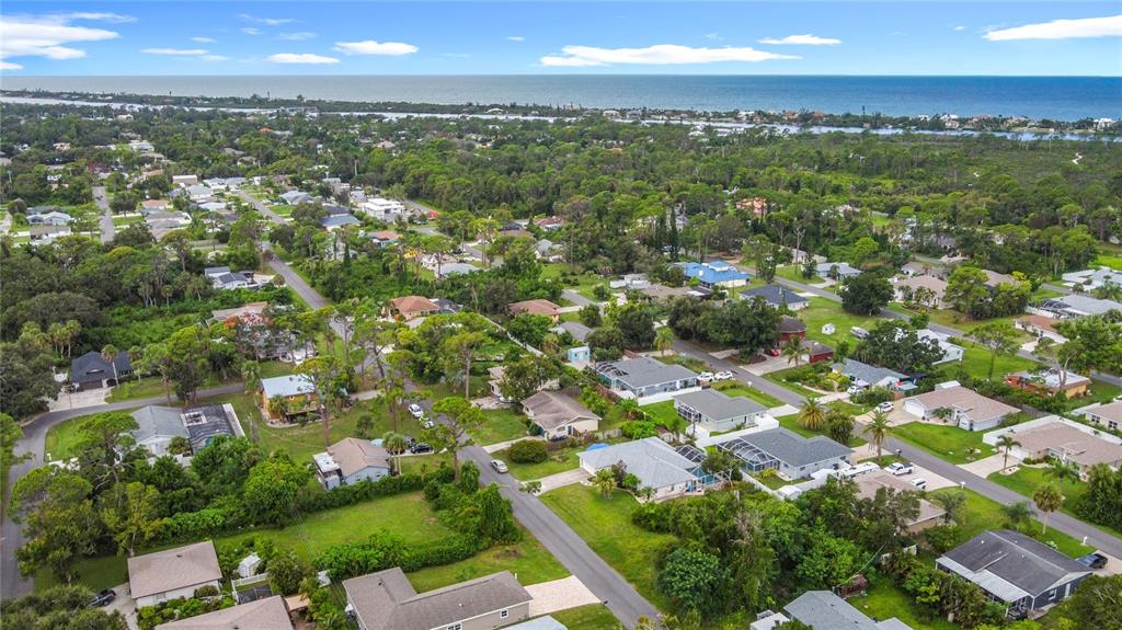 An aerial view shows a suburban neighborhood with houses, trees, and the ocean in the distance — 5964 DIANA ROAD, VENICE, FL