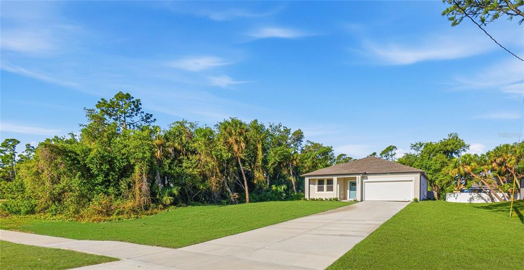 A single-story house with a white garage and light-colored siding sits beside dense trees — 5131 S SAN MATEO DRIVE, NORTH PORT, FL
