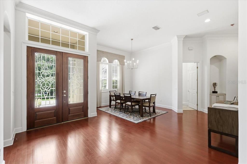 A dining area features hardwood floors, a chandelier, and double front doors with glass inserts — 6124 FOXFIELD COURT, WINDERMERE, FL