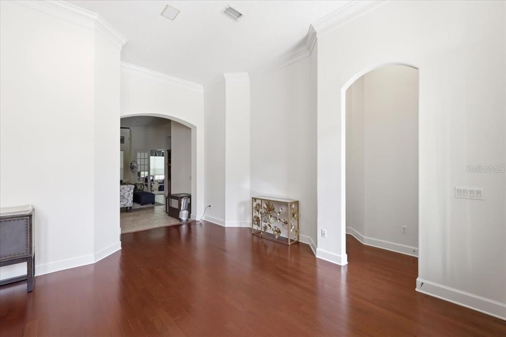 A room with hardwood floors, white walls, crown molding, and two arched doorways — 6124 FOXFIELD COURT, WINDERMERE, FL
