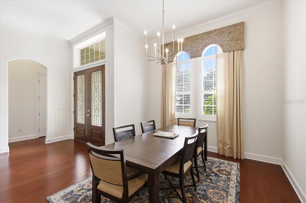 A dining room features a dark wood table, chandelier, arched windows, and hardwood flooring — 6124 FOXFIELD COURT, WINDERMERE, FL