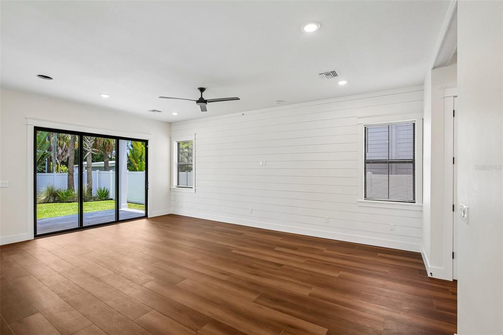 A living room features white shiplap walls, wood-look flooring, a ceiling fan, and sliding glass doors — 3819 71ST STREET N, ST PETERSBURG, FL
